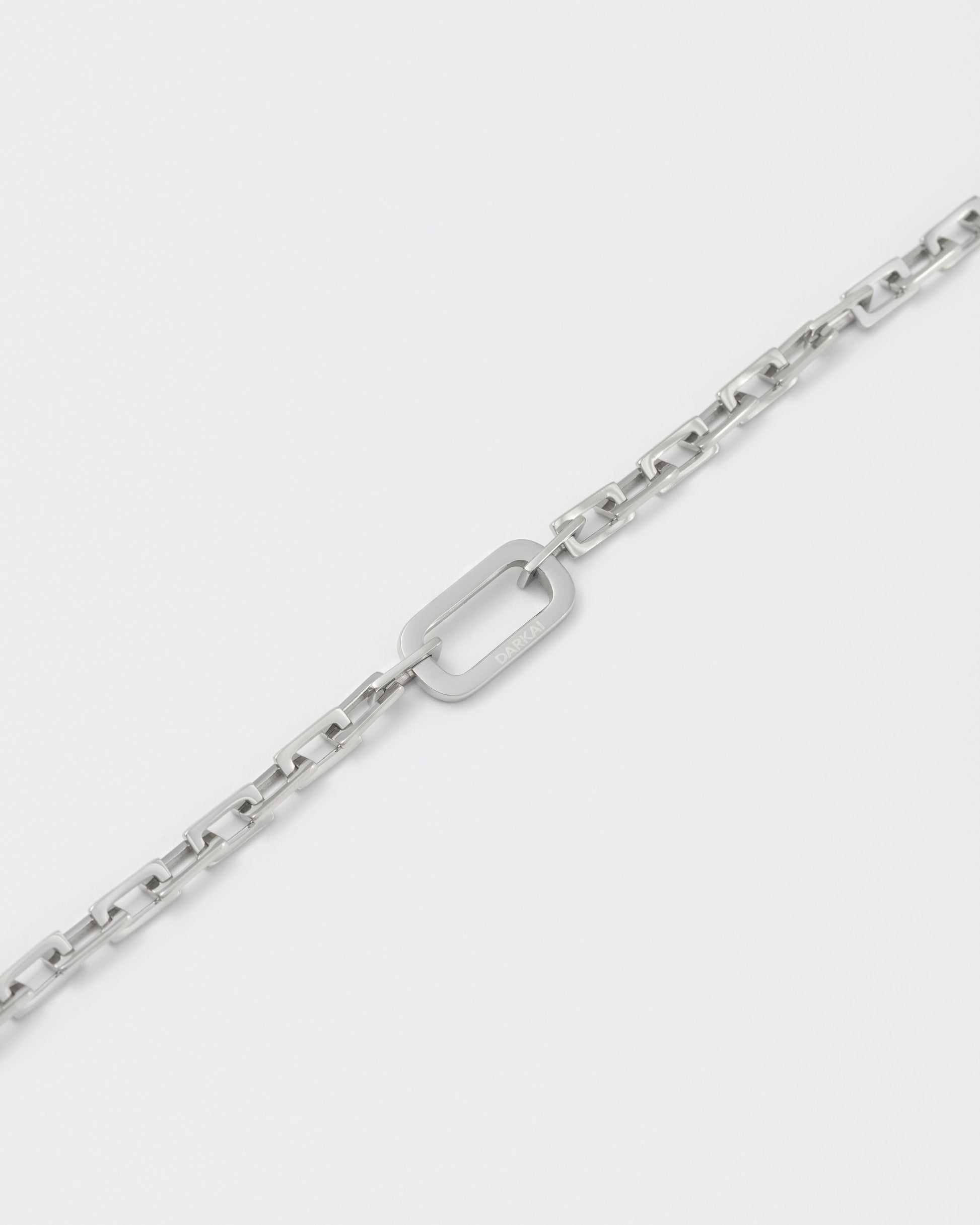 detail of 18k white gold coated edgy diamond finished rolo chain bracelet with central oval link detail and lobster clasp with logo