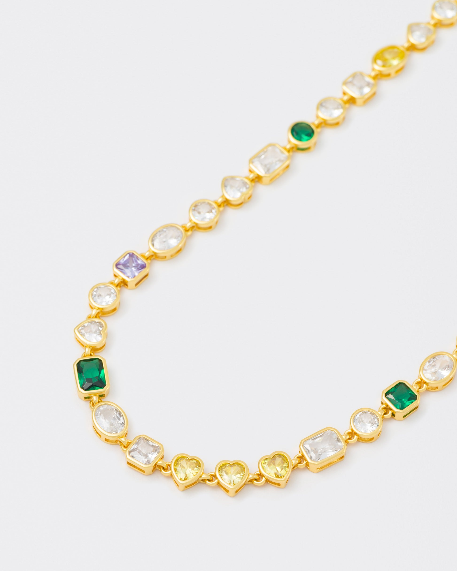 detail of 18k yellow gold coated mixed bezels chain bracelet with hand-set stones in different shapes and colors. Mix of rectangular, square, round and heart-shaped stones in white, amethyst, emerald green and golden yellow
