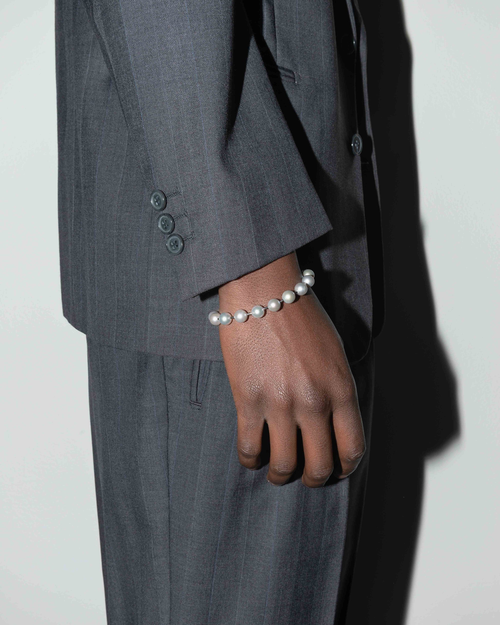 street style man wearing Natural Indonesian freshwater pearls bracelet with ematite spacers and 18k white gold coated carabiner clasp with logo. 9mm natural freshwater pearls in silver grey.