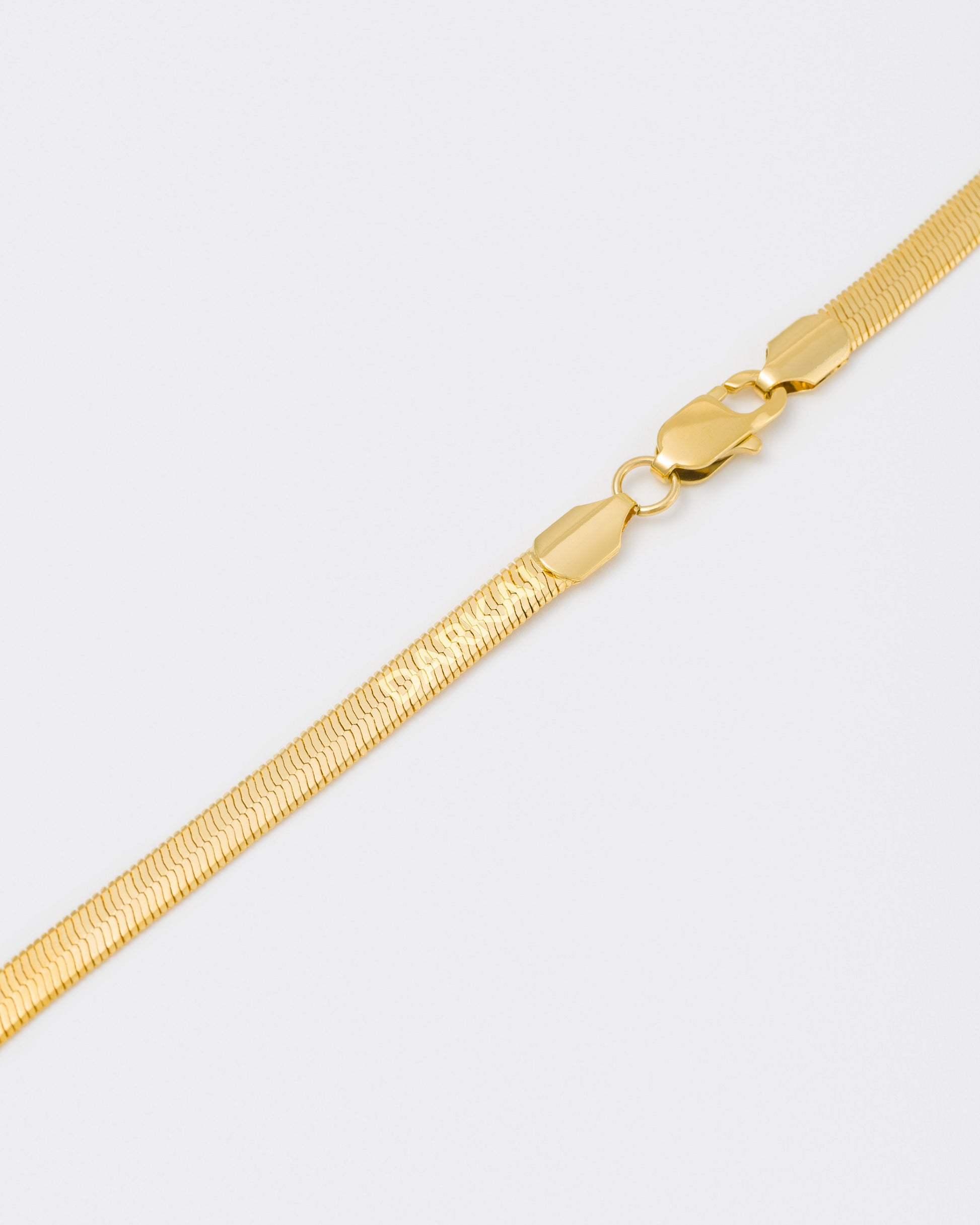 detail of 18k yellow gold coated herringbone chain necklace with lasered logo along the links and regular lobster clasp.