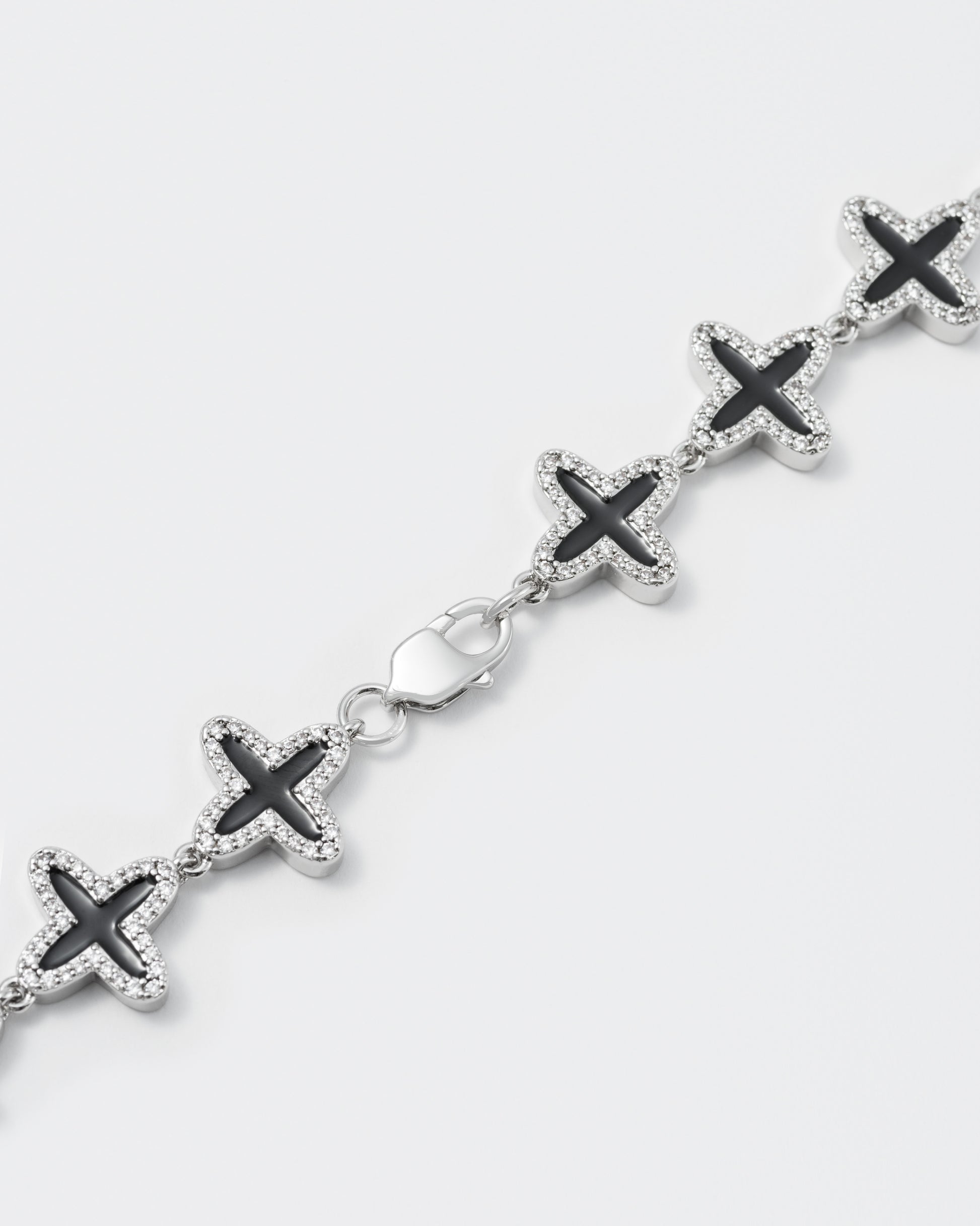 detail of clover tennis chain bracelet with 18kt white gold coating and hand-set stones in diamond white. Finished with hand painted black enamel and lobster clasp with logo