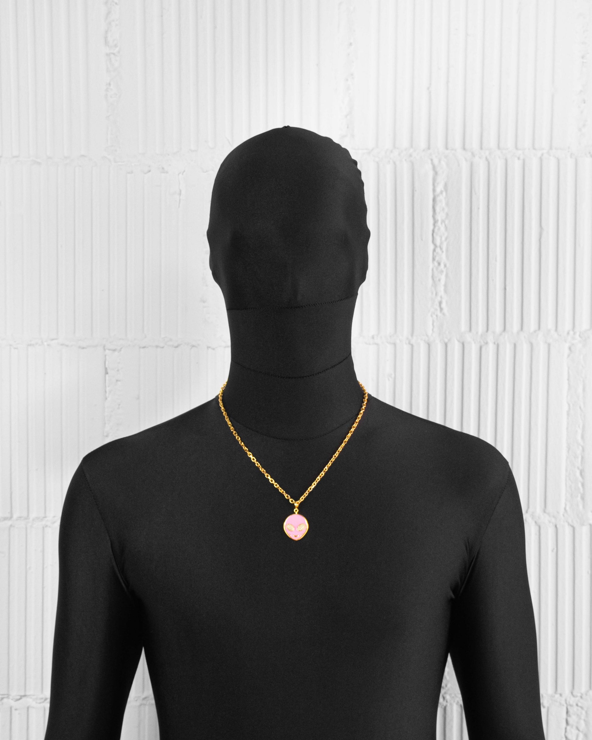 man with black suit wearing 18k yellow gold coated alien pendant necklace with hand-set micropavé stones in pink hand painted glow in the dark alien pendant and 3mm rolo chain