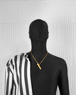 man with black suit wearing 18k yellow gold coated vial pendant necklace with hand-set micropavé stones in white, matte/satined finishing and 3mm rolo chain