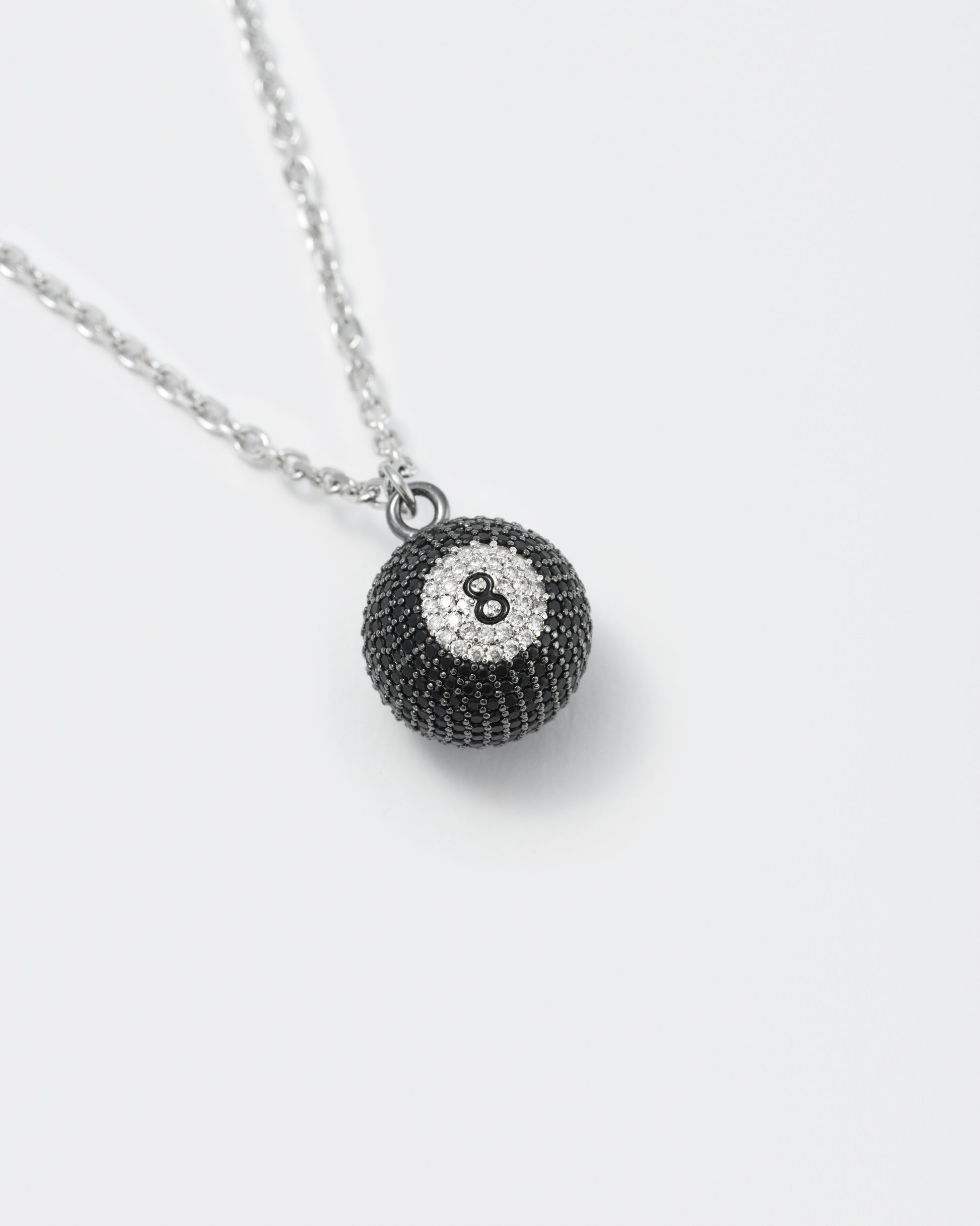 detail of eight ball pendant necklace with deep black PVD coating and hand-set micropavé stones in black and diamond white. Hand painted number 8 in black enamel. 2mm cable chain and lobster clasp with metal logo tag