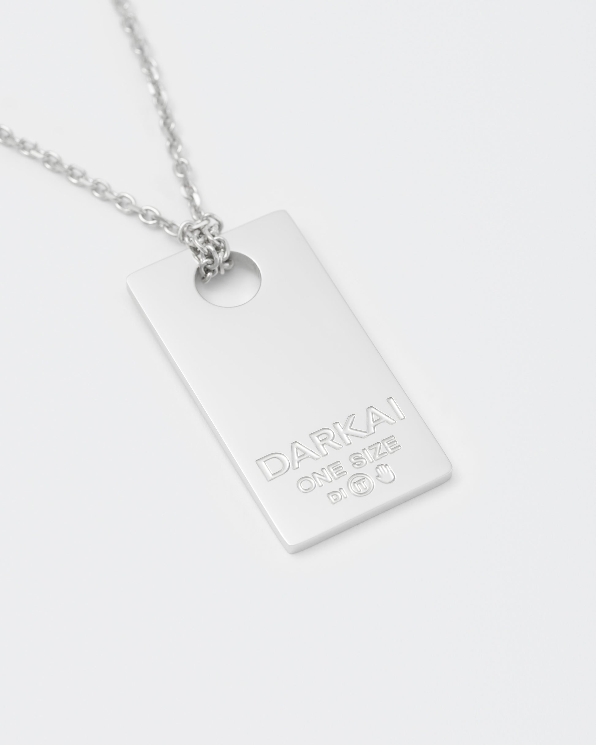 detail of size tag pendant necklace with 18kt white gold coating with lasered logo and details. 2mm cable chain and lobster clasp with metal logo tag.
