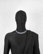 man with black suit wearing 18k white gold coated prong chain necklace with hand-set micropavé stones in gradient white, brazil green, green, aquamarine, tanzanite and sapphire blue