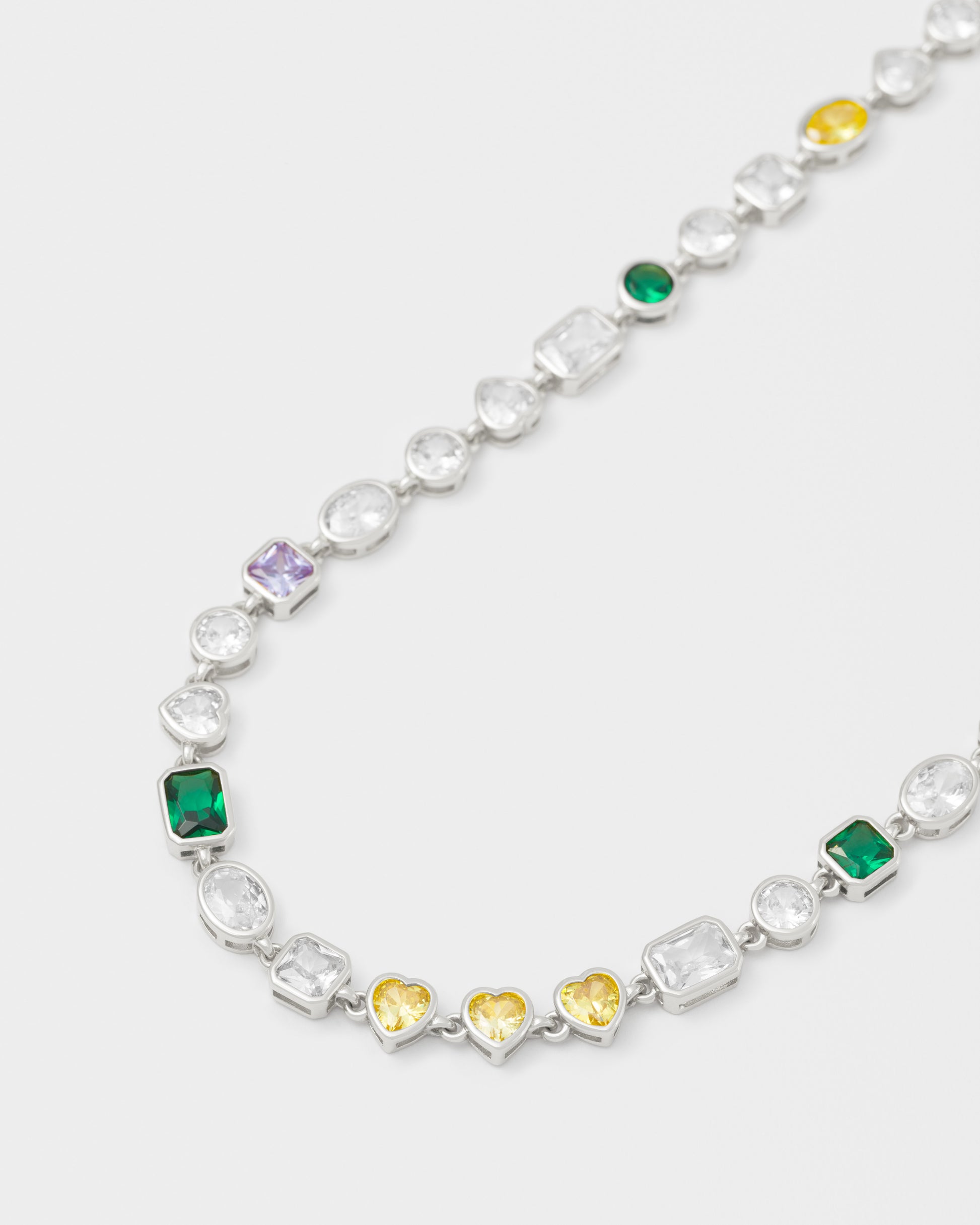 detail of mixed bezels chain necklace with 18kt white gold coating and hand-set stones of irregular shapes and colors. Ensemble of rectangular, square, round and heart-shaped stones in diamond white, amethyst, lilac, emerald green and gold yellow. Invisible closure with logo.