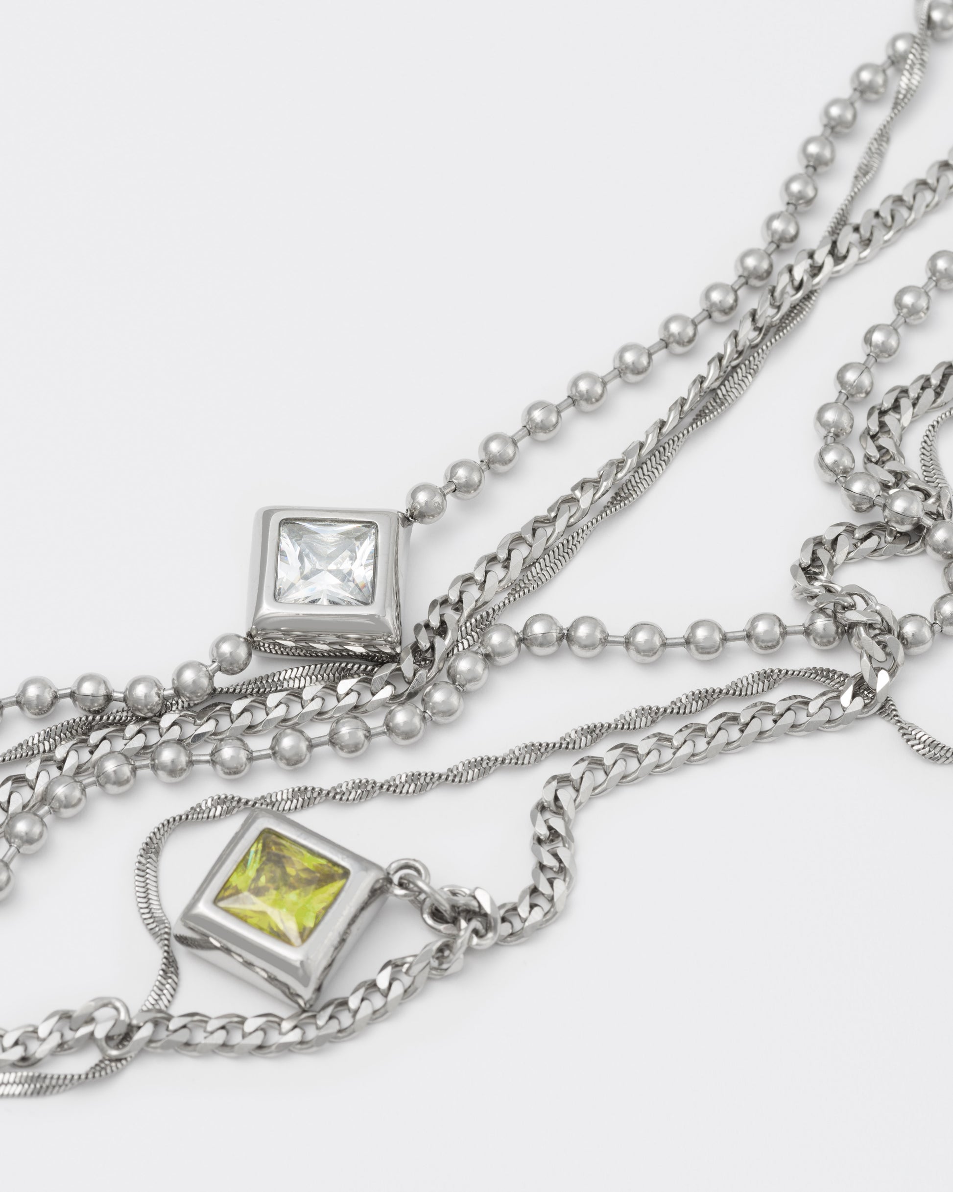 detail of triple layer chain necklace with 18kt white gold coating and rhombus shaped pendants with princess-cut stones in diamond white, sapphire blue, olive and dark champagne