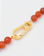detail of clasp of Amber stones necklace with 18k yellow gold coated lasered logo oversize carabiner clasp.