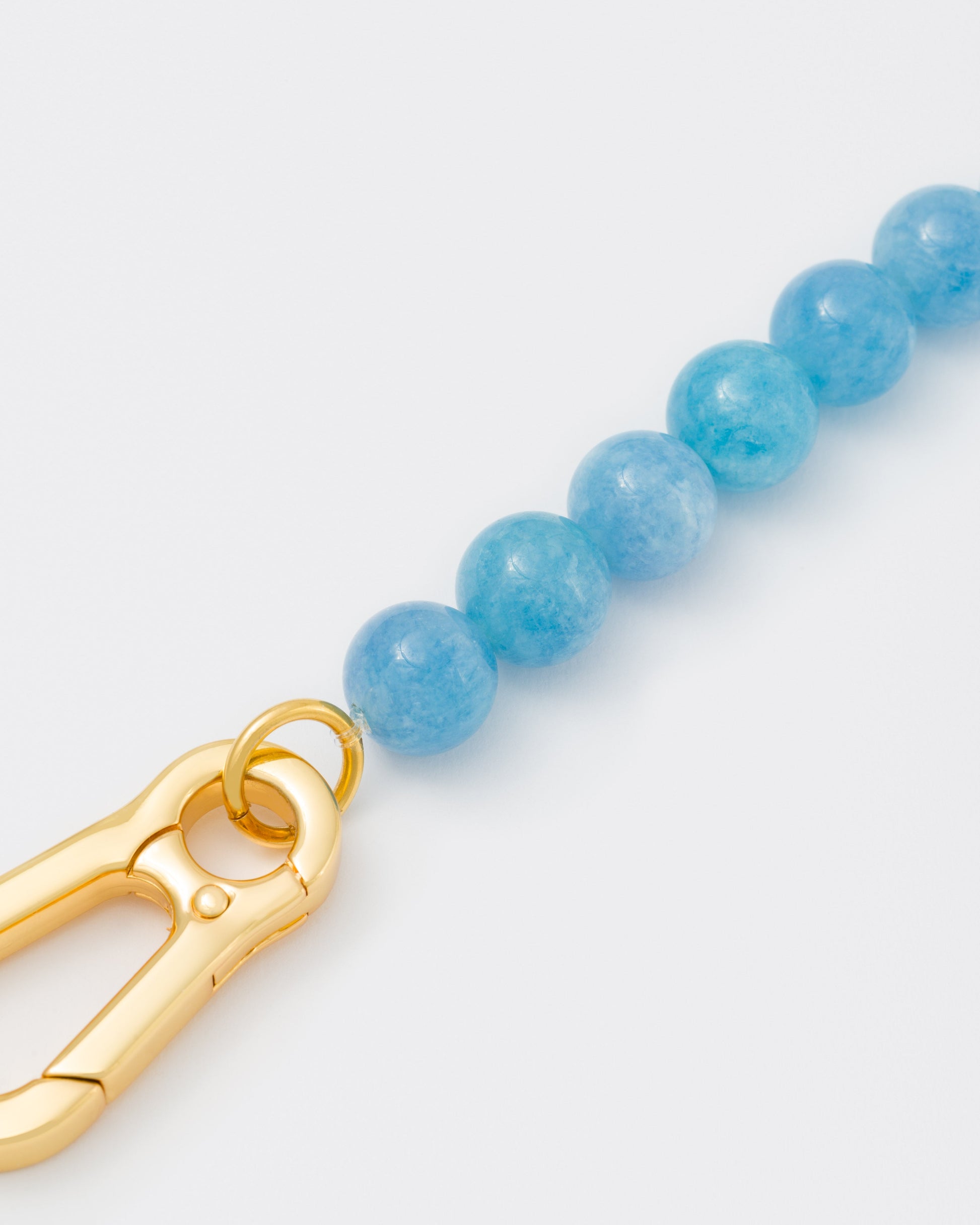 detail of Aquamarine stones necklace with 18k yellow gold coated lasered logo oversize carabiner clasp.