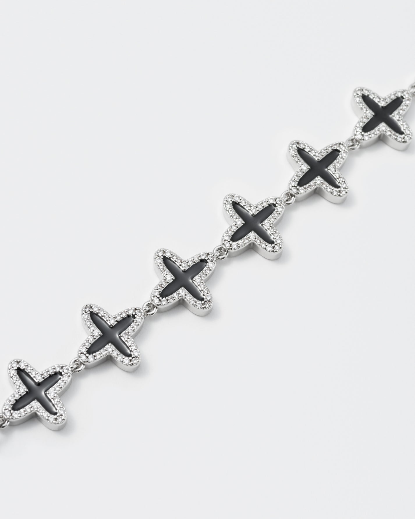 detail of clover tennis chain necklace with 18kt white gold coating and hand-set stones in diamond white. Finished with hand painted black enamel and lobster clasp with logo