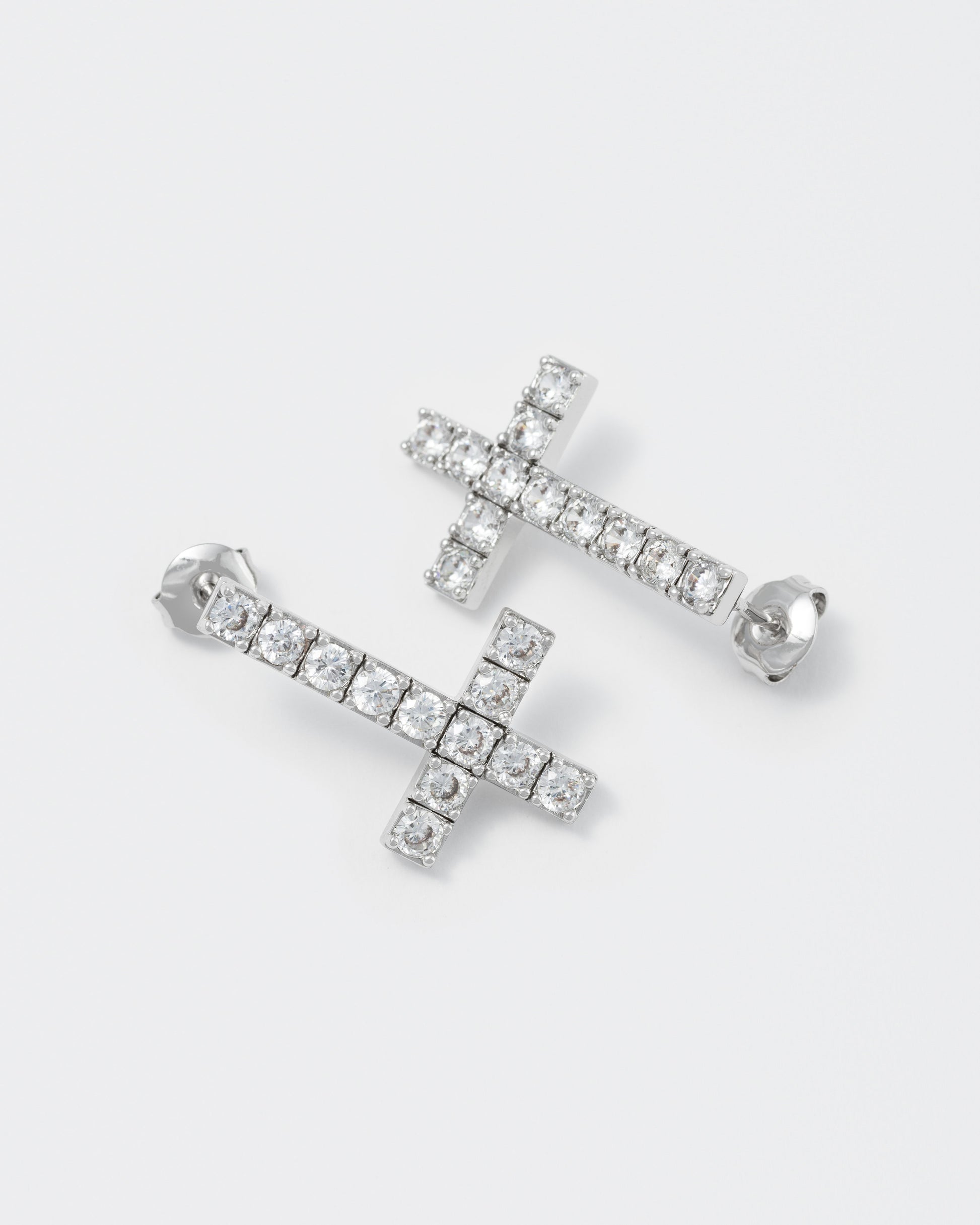 detail of reversed cross earrings with 18kt white gold coating with round brilliant-cut stones in diamond white. Silver 925 pin and butterfly closure with logo